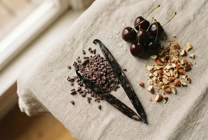 Cocoa nibs, a split vanilla pod, dark cherries and toasted almonds on a linen cloth, the edible notes the gourmand originals list