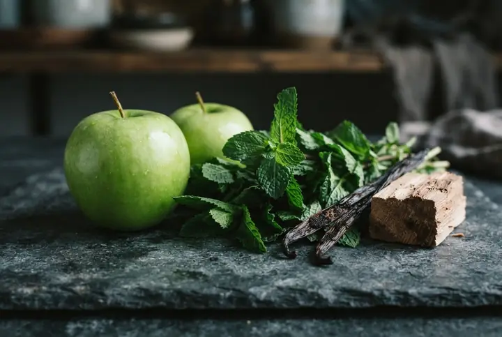Green apples, fresh mint leaves, a split vanilla pod and a block of cedar wood on dark stone, notes on the Versace Eros list